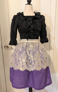 photo of mannequin wearing a black blouse and purple skirt with a gold lace apron on top