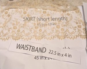 photo of the gold lace fabric on top of the apron pattern with the waistband placed on top for comparison