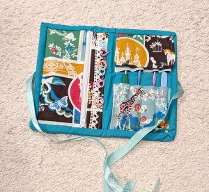 handmade fabric sewn crochet tool kit opened with some hooks and stitch markers displayed