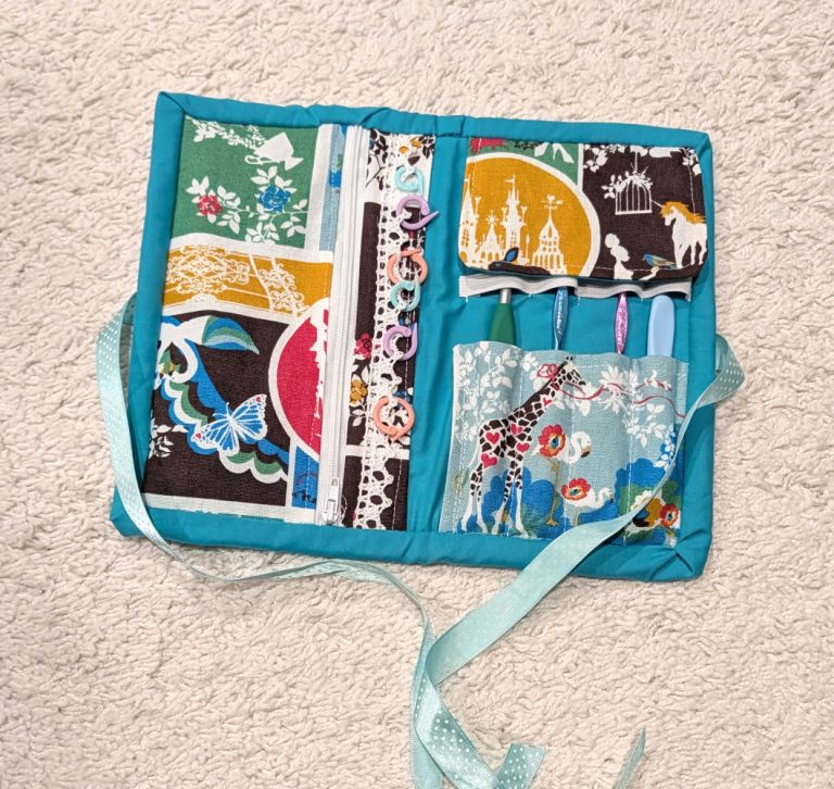 handmade fabric sewn crochet tool kit opened with some hooks and stitch markers displayed