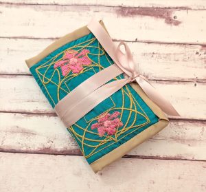 the front of the embroidered husswif, with design patterened by sewstine, tied with pink satin ribbon