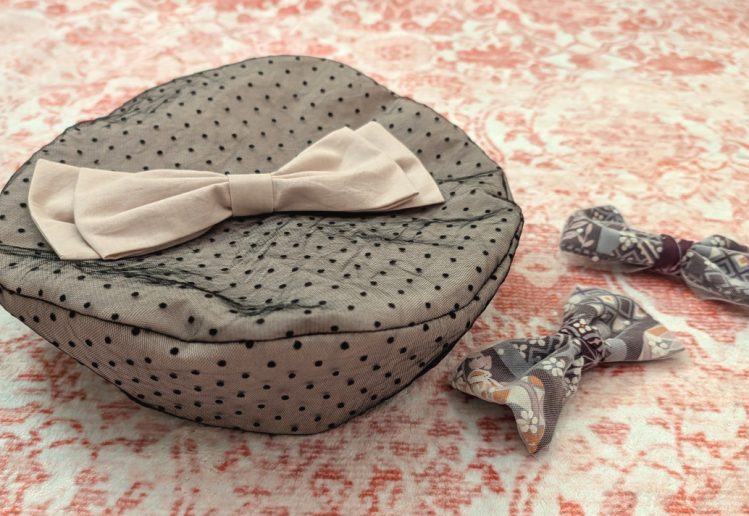 photograph of a handmade fabric beret sewn from pink fabric overlaid with black polkadot lace and decorated with a pink fabric bow, next to two purple/pink/white Japanese print bows