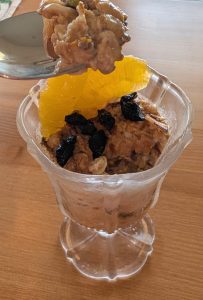 photograph of glass filled with overnight oats garnished with dried cherries and orange slices and pistachios
