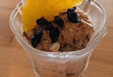 photograph of glass filled with overnight oats garnished with dried cherries and orange slices and pistachios