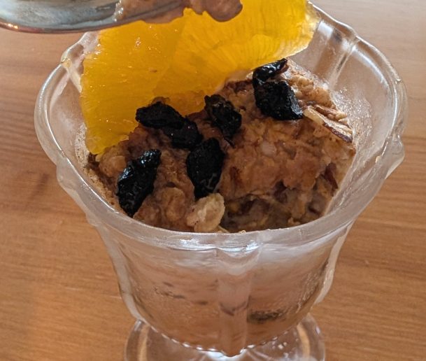 photograph of glass filled with overnight oats garnished with dried cherries and orange slices and pistachios