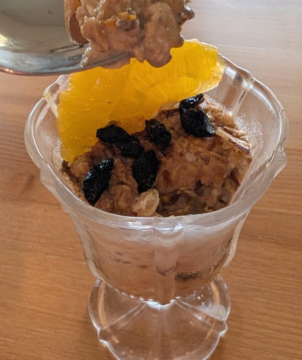 photograph of glass filled with overnight oats garnished with dried cherries and orange slices and pistachios