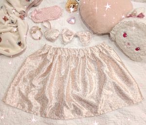 photograph of pink/white satin leopard print skirt with matching bow and heart ornament, surrounded by other cute pink items