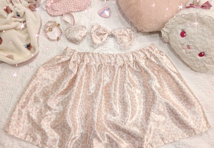 photograph of pink/white satin leopard print skirt with matching bow and heart ornament, surrounded by other cute pink items