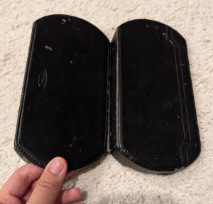 PSP handheld console case that is probably 20 years old, peeling black fake leather, cracks in the plastic