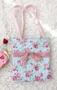 photograph of a blue/pink floral print tote bag with a pink lace bow