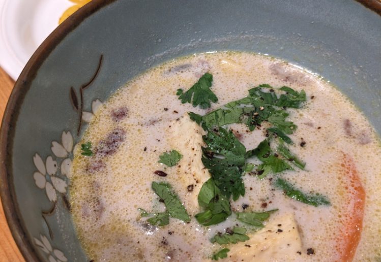 photo of a bow of coconut milk fish and tofu stew, with fried plantains in the background