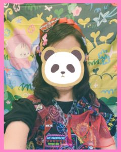 closeup photo of Meta's Cyber Neon Girl dress worn against the summer camp background of Sprinkle Trinkle Town art market. A panda sticker is placed over the face