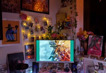 photograph of PC setup featuring pink Razer accessories and Final Fantasy Tactics, 7 and 9 official and fan merch. with the main light turned off