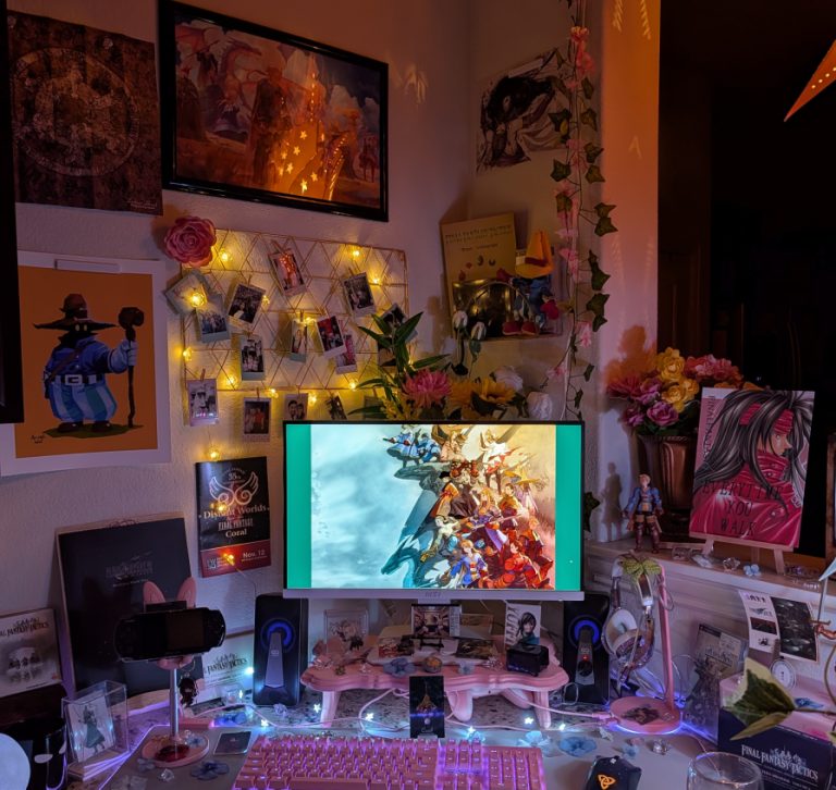 photograph of PC setup featuring pink Razer accessories and Final Fantasy Tactics, 7 and 9 official and fan merch. with the main light turned off