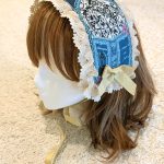 photograph of handmade headdress trimmed with lace and ribbons on a wig head wearing a brown wig