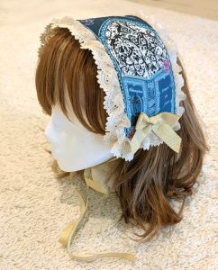 photograph of handmade headdress trimmed with lace and ribbons on a wig head wearing a brown wig