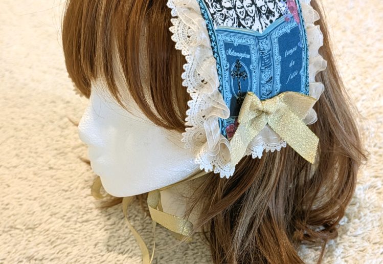 photograph of handmade headdress trimmed with lace and ribbons on a wig head wearing a brown wig