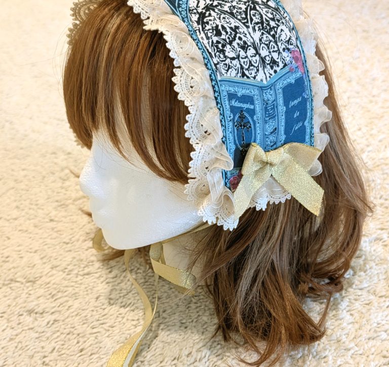 photograph of handmade headdress trimmed with lace and ribbons on a wig head wearing a brown wig